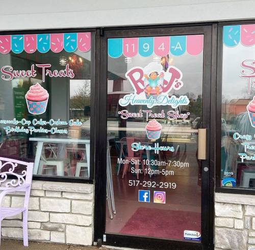 Exterior of a dessert shop with a colorful sign, featuring cupcakes and sweet treats, and store hours displayed.