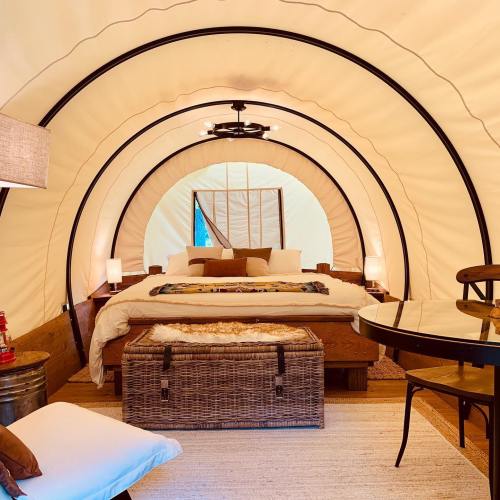 Cozy glamping tent interior with a bed, decorative pillows, a table, and warm lighting.