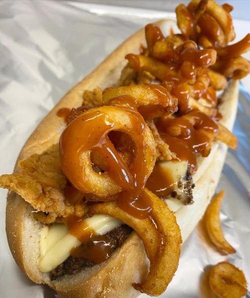 A loaded hot dog topped with crispy fried chicken, curly fries, and drizzled with barbecue sauce.