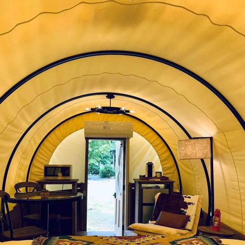 Interior of a cozy, curved tent with a door, furniture, and a small kitchenette, surrounded by warm yellow tones.