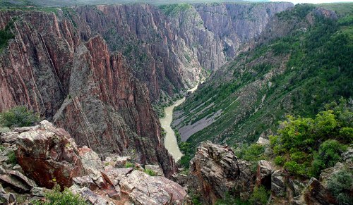 A dramatic canyon with steep, rocky cliffs and a winding river at the bottom, surrounded by lush greenery.