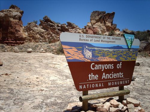 Sign for Canyons of the Ancients National Monument, with rocky terrain and blue sky in the background.