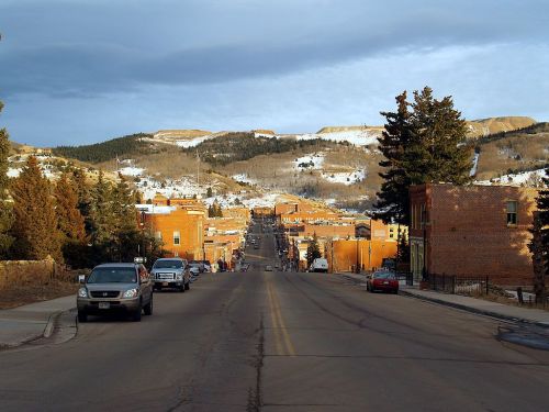A view down a street lined with brick buildings, leading to snow-capped mountains under a cloudy sky.