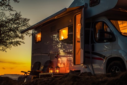 A cozy camper van at sunset, with warm lights glowing from the windows and chairs set outside.