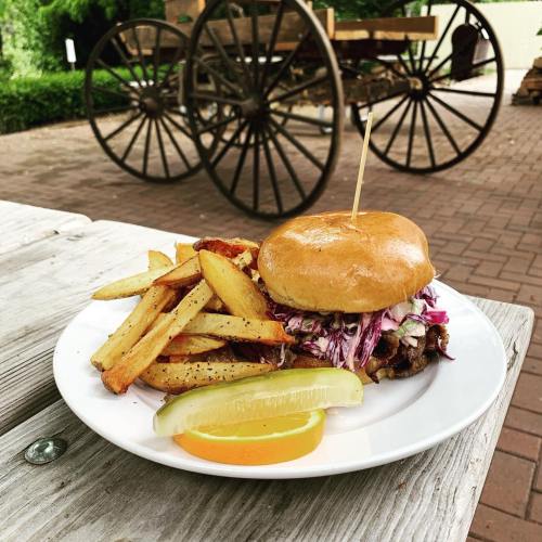 A plate with a burger topped with slaw, served with golden fries and a slice of lemon, set against a rustic background.