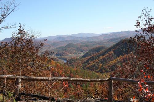 Scenic view of colorful autumn mountains with a wooden railing in the foreground under a clear blue sky.