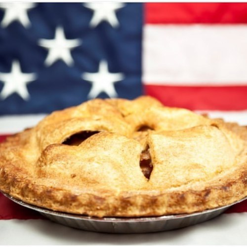 A golden-brown apple pie in front of an American flag backdrop.