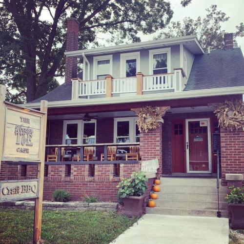 A cozy brick building with a sign reading "The Tasty Cafe," featuring outdoor seating and autumn decorations.
