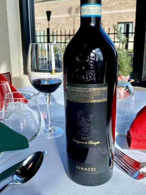 A bottle of 2017 Tinazzi wine on a table, accompanied by a glass of red wine and festive table settings.