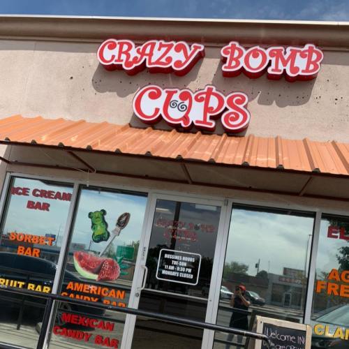 Sign for "Crazy Bomb Cups" featuring various dessert options like ice cream, sorbet, and candy bars. Bright, inviting storefront.