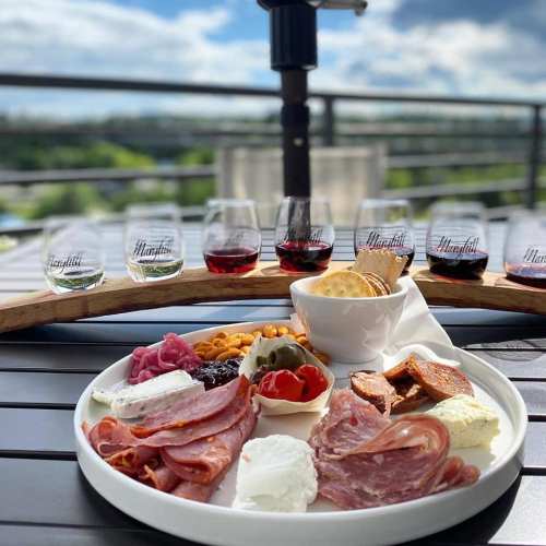 A platter of assorted meats, cheeses, olives, and dips, accompanied by glasses of wine on a sunny balcony.