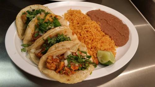 A plate of tacos filled with meat and topped with cilantro, served with rice, refried beans, and a lime wedge.