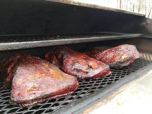 Smoked briskets resting on a grill, showcasing a rich, dark bark and juicy texture.