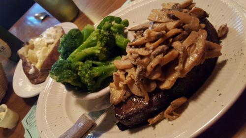 A plate featuring a steak topped with mushrooms, served with broccoli and a baked potato on the side.