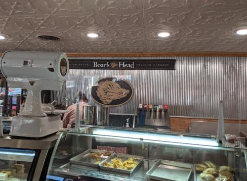 A deli counter featuring Boar's Head products, with a scale and food display in a cozy, vintage-style setting.