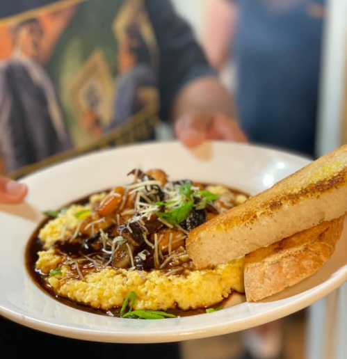 A plate of creamy grits topped with shrimp and sauce, garnished with herbs, alongside two slices of toasted bread.