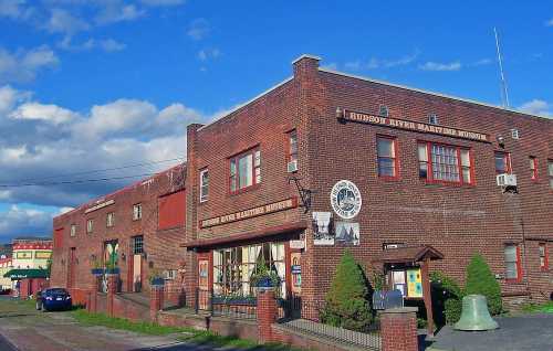 Brick building with a sign for the Hudson River Maritime Museum, surrounded by greenery and under a blue sky.