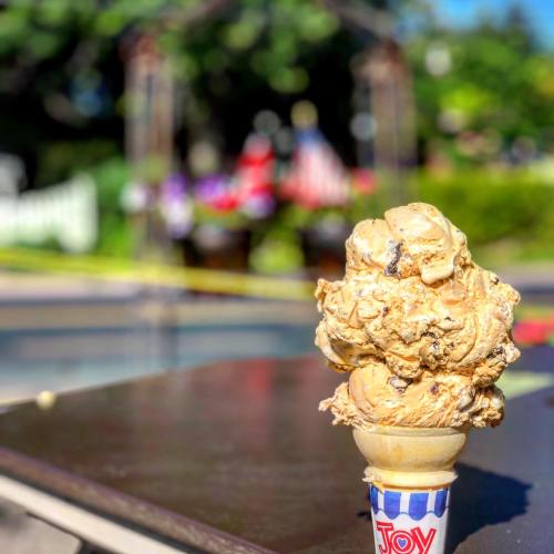 A close-up of a large ice cream cone with caramel swirls, set against a blurred outdoor background.