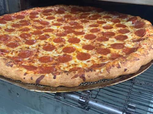 A freshly baked pepperoni pizza with a golden crust, sitting on a pizza rack in an oven.