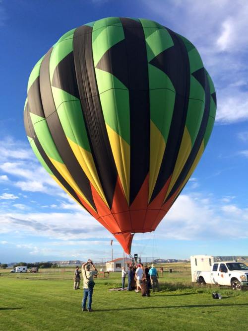 A colorful hot air balloon is being prepared for flight on a grassy field under a blue sky with scattered clouds.