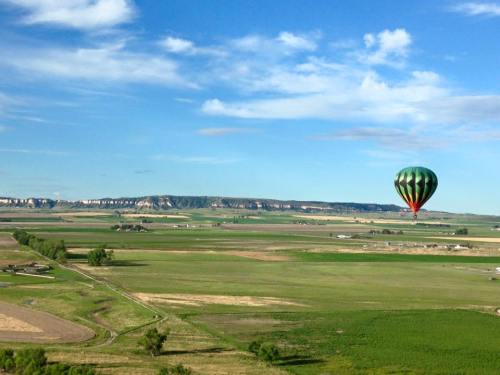 A colorful hot air balloon floats over a vast green landscape with rolling hills and a clear blue sky.