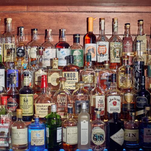 A variety of liquor bottles displayed on a wooden shelf, including whiskey, gin, and vodka.