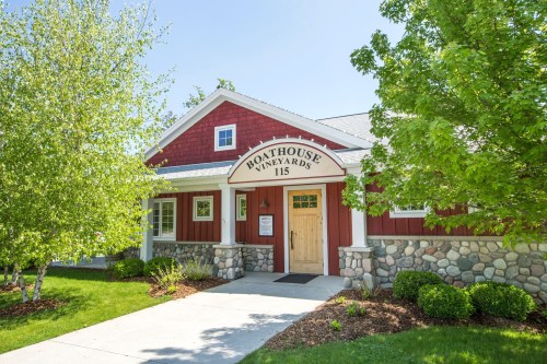 A charming red and stone building with a sign reading "Boathouse Vineyards," surrounded by greenery and trees.