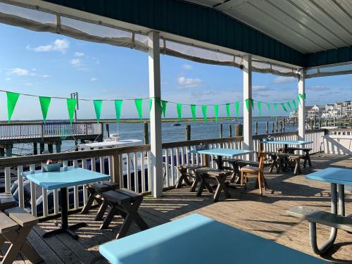 Outdoor dining area with turquoise tables, green bunting, and a view of the water and boats in the background.