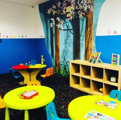 Colorful playroom with a forest mural, tables, chairs, and storage cubbies, designed for children's activities.