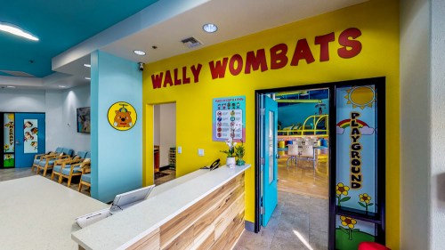 Brightly colored entrance to "Wally Wombats" with a reception desk and a view of a playful indoor playground.