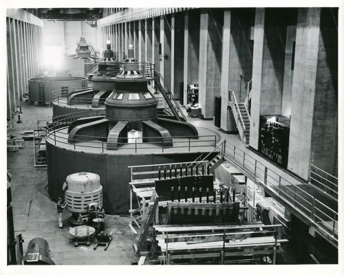 Black and white image of large industrial turbines in a spacious, concrete facility.