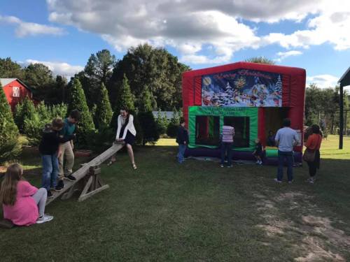 A colorful bounce house with children playing nearby, surrounded by trees and a clear blue sky.