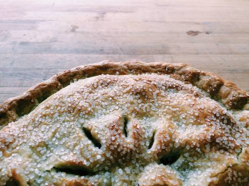 Close-up of a golden-brown pie crust topped with sparkling sugar, resting on a wooden surface.