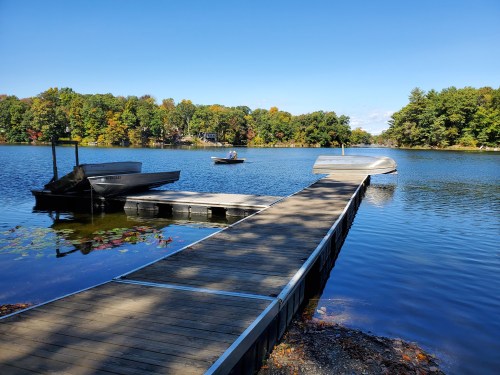 A wooden dock extends into a calm lake, with boats moored and colorful trees reflecting in the water.