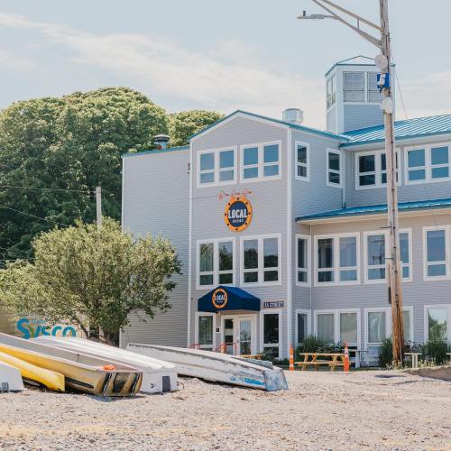 A modern building with a blue roof and "Local" sign, surrounded by trees and parked kayaks in the foreground.