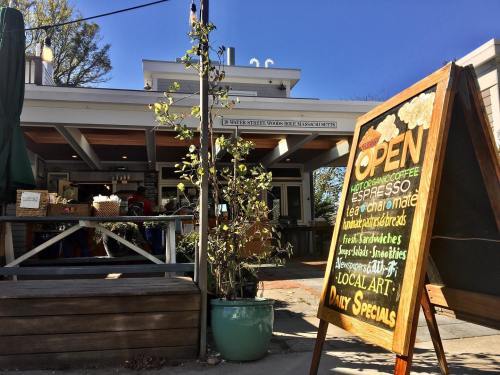 A cozy café with an open sign, outdoor seating, and a chalkboard displaying daily specials and local art.