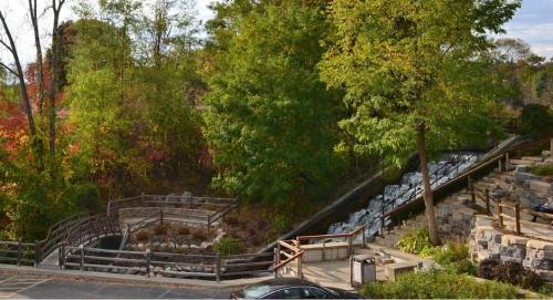 A serene landscape featuring a waterfall, lush greenery, and a wooden walkway in a park setting.