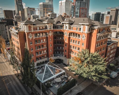 Aerial view of a historic red brick building with modern city skyline in the background and a glass-roofed patio area.
