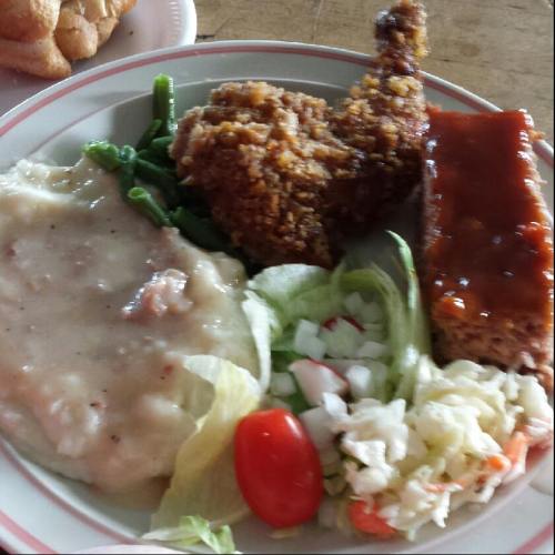 A plate of fried chicken, meatloaf with sauce, green beans, mashed potatoes, salad, and coleslaw.