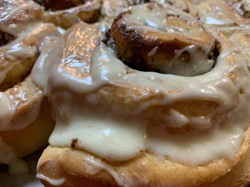 Close-up of freshly baked cinnamon rolls topped with creamy icing, showcasing their soft, gooey texture.