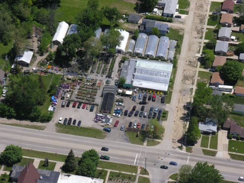 Aerial view of a garden center with greenhouses, parking lot, and surrounding residential area.