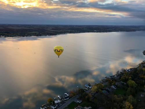 A colorful hot air balloon floats over a calm lake at sunset, reflecting the sky's hues on the water's surface.