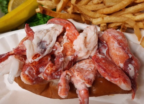 A lobster roll topped with fresh lobster meat, served with a side of fries and a lemon wedge.
