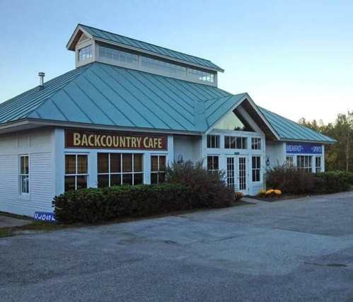 Exterior of Backcountry Cafe with a blue metal roof and large windows, surrounded by greenery and a clear sky.
