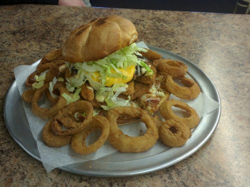 A large burger topped with lettuce and cheese, surrounded by crispy onion rings on a metal plate.