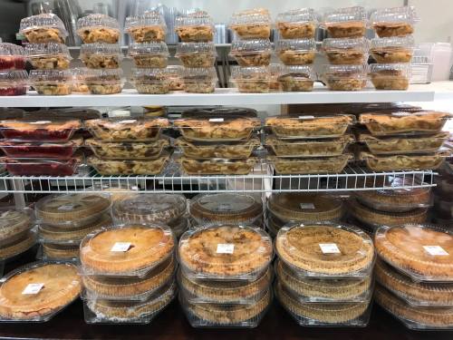 A display of various pies in clear plastic containers, stacked on shelves and arranged neatly.
