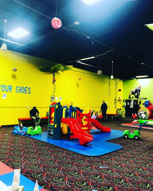 Brightly colored indoor play area with slides, toy cars, and a vibrant yellow wall. Children play in a fun, safe environment.