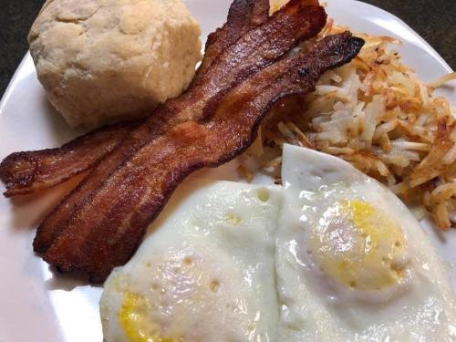 A plate of breakfast featuring crispy bacon, fried eggs, hash browns, and a biscuit.