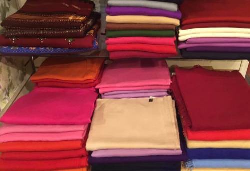 A display of neatly stacked colorful fabrics in various shades, arranged on shelves.