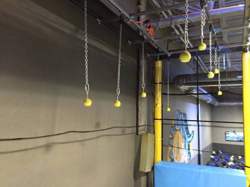 A view of a trampoline park featuring hanging yellow balls and a blue safety mat below.